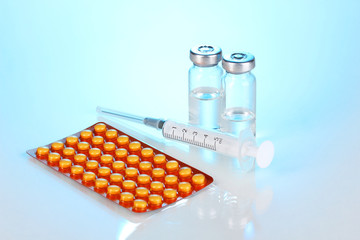 Syringe with medical ampoules and tablets on blue background