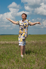 Happy mature woman standing in the field under blue sky arms wid
