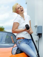 Pretty woman is loading electrically powered car outdoors
