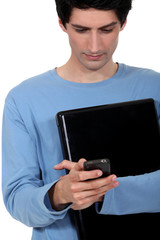 A casual young man with a laptop and a cellphone.