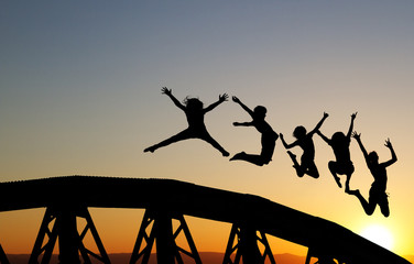 silhouette of teenagers jumping on bridge in sunset