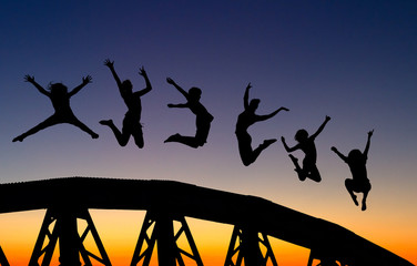 silhouette of teenagers jumping on bridge in sunset