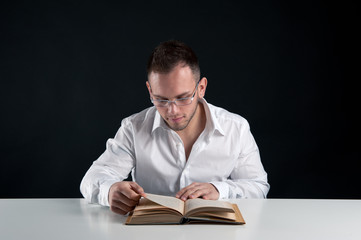 Young man reading a book against black background.