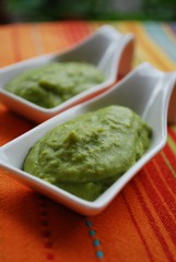 Green broad beans cream in white china dish on orange background