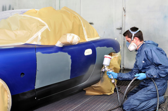 Worker painting a blue car.