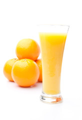 Heap of oranges behind a glass of orange juice