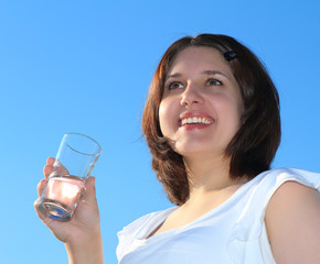 Young woman drinking water on sky background