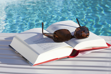 Sunglasses on a book by the swimmingpool