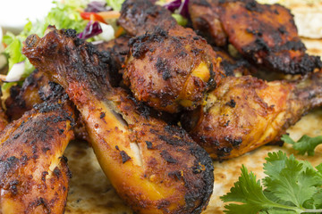 Tandoori Chicken Legs on top on a Naan Bread with salad.