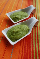 Green broad beans cream in white china dish on orange background