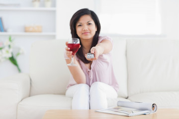 Obraz na płótnie Canvas Woman holding a television remote and a glass of red wine