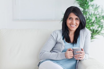 Smiling woman holding a mug with two hands while resting on a so