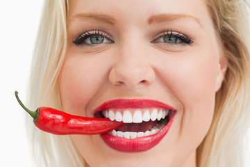 Happy blonde woman biting a red chili pepper