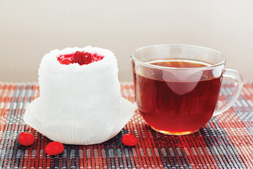 Cup of tea and cream cake with cherries on a bamboo table cloth