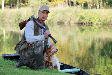 A hunter and his dog by a river.