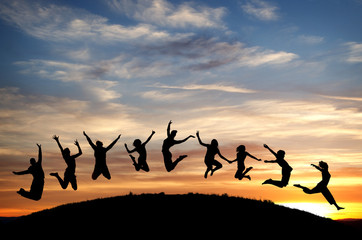 silhouetted teenagers jump on hill in sunset