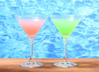 Glasses of cocktails on wooden table on blue sea background