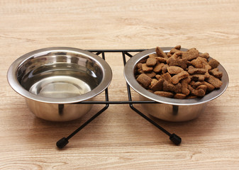 dry dog food and water in metal bowls on wooden background