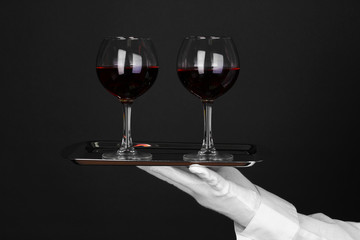 Hand in glove holding silver tray with wineglasses isolated