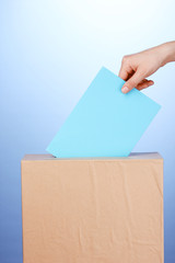 Hand with voting ballot and box on blue background