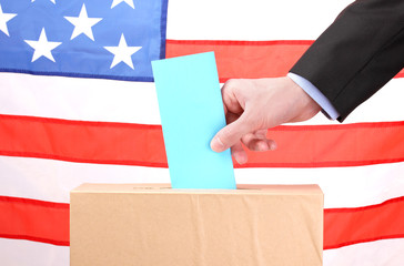 Hand with voting ballot and box on Flag of USA