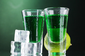 Two glasses of absinthe, lime and ice on green background