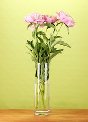 Three pink peonies in vase on wooden table on green background
