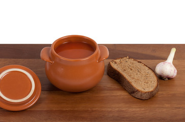Soup in ceramic pot with bread and garlic