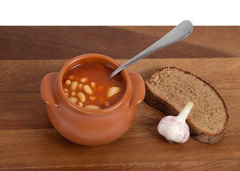 Soup in ceramic pot with bread and garlic on wooden table