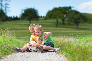 Zwei Kinder mit Fußball sitzen auf einem Feldweg © Kzenon