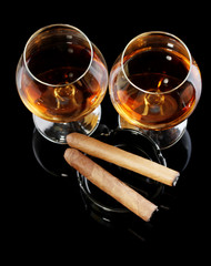 two glasses of brandy and cigars on black background