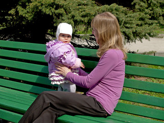 Молодая женщина с младенцем сидят на скамейке в парке