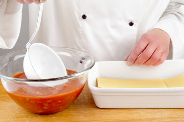 female chef with tomato sauce preparing lasagna