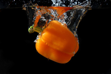 Orange pepper dropped in water with black background