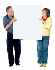 Mature couple presenting blank white billboard