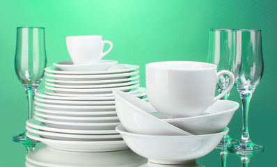 Clean plates, cups and glasses on green background
