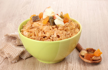 tasty cornflakes in bowl with dried fruits on wooden table