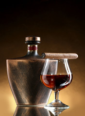 bottle and glass of brandy and cigar on brown background