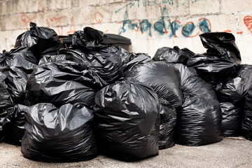 Tied black garbage bags in a city street - obrazy, fototapety, plakaty