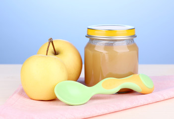 Jar of baby puree with spoon on napkin on blue background