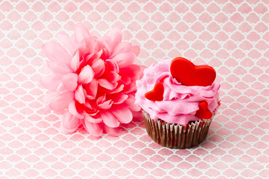 a pink flower beside a pink cupcake with hearts in it