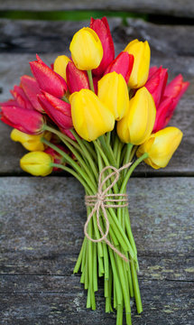 tied yellow and red tulips on wooden surface
