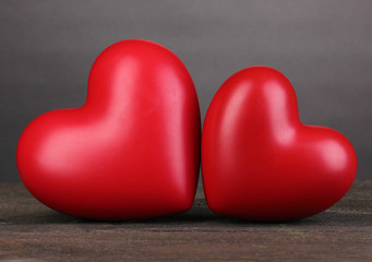 Two decorative red hearts on wooden table on grey background