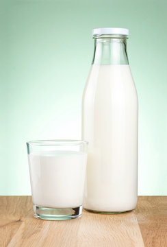 Bottle of fresh milk and glass is wooden table on a green backgr