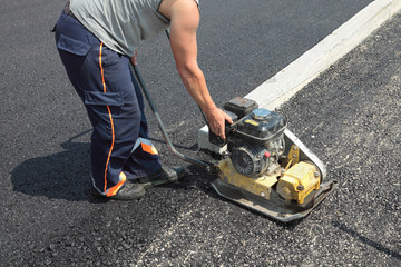 Roadworks, worker with  compactor at asphalt