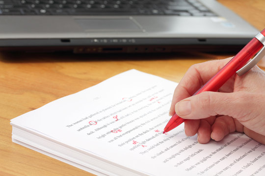 Hand with red pen proofreading  by laptop