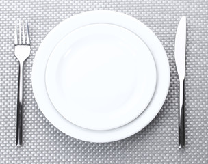 White empty plates with fork and knife on a grey tablecloth