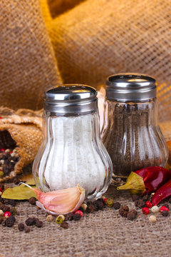 Salt and pepper mills and spices on burlap background