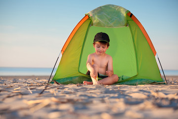 Little boy playing in his tent on the beach