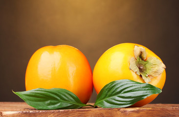 Two appetizing persimmons on wooden table on brown background